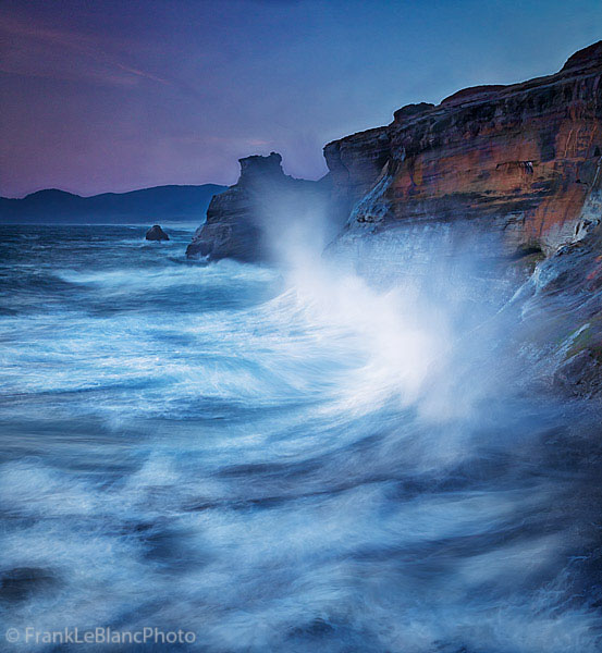 The setting sun joined by roaring waves as they explode against the shore cliffs. Photographed from above and at a distance....