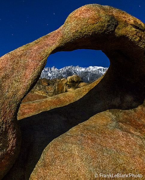Looking through Mobius Arch toward the snow covered Eastern Sierra Nevada at night.