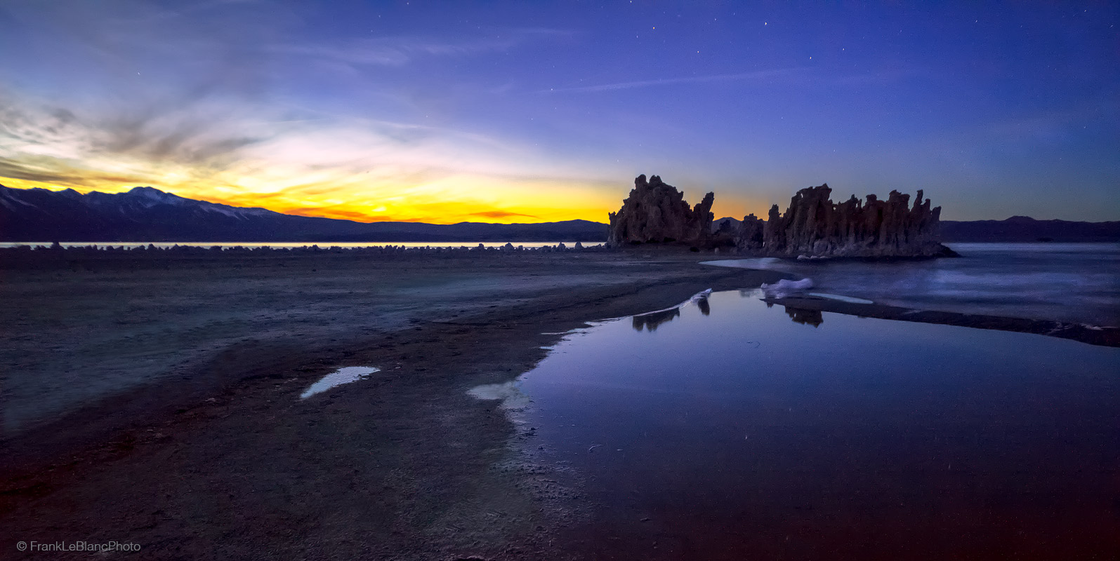 Dusky clouds dissipate over the sierra and scatter outward over the lake while sunset light intensifys over Lee Vining to the...