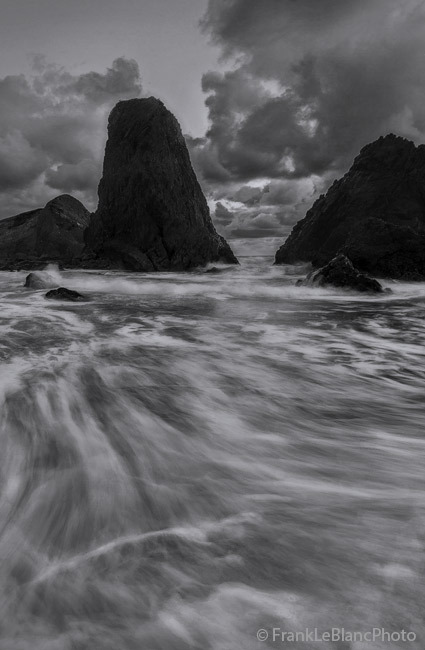 Incoming tide creates rushing waves pouring between sandstone towers. Water surges forward with driving force. Look close, and...